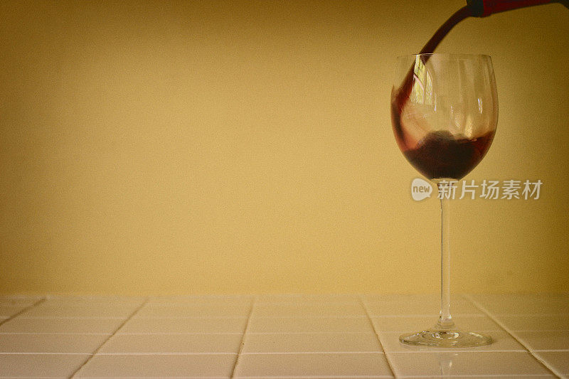 红酒倒入瓷砖柜台上的玻璃杯中