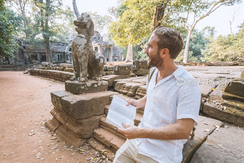 一个年轻人正在柬埔寨的古庙里阅读旅游指南