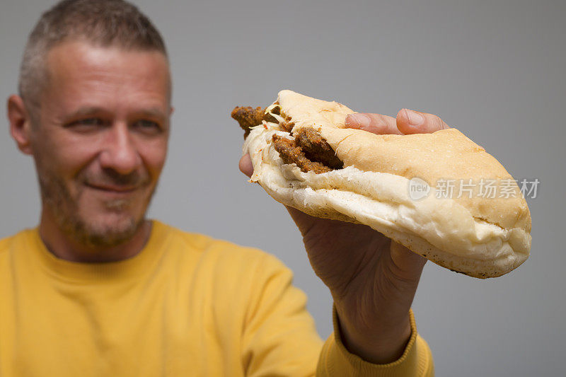 饥饿的大人捧着炸肉排中的小圆面包，准备吃