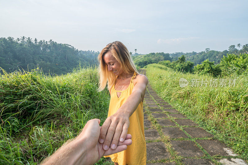 跟随我的概念年轻女子带领男友到稻田在Campuhan岭漫步在巴厘岛，亚洲人旅游奇迹分享爱的概念-