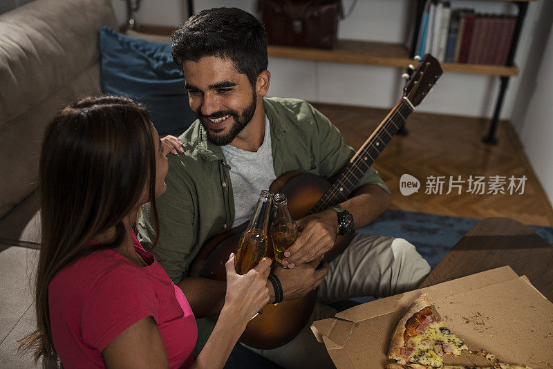 快乐的年轻女孩享受而听她的男朋友在家里弹吉他。