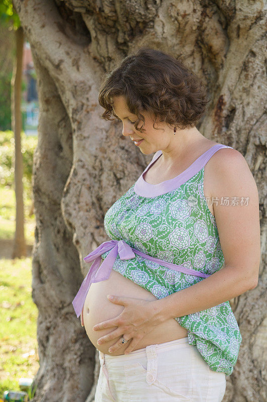 女人在老树前发光，露出怀孕的肚子