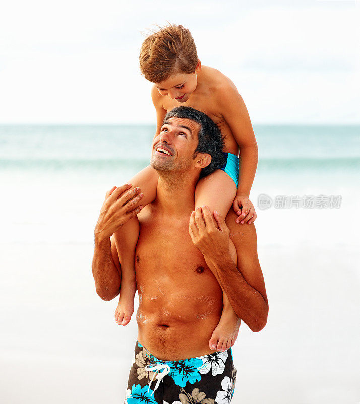 在海滩上，一个男人背着他的儿子，互相看着对方