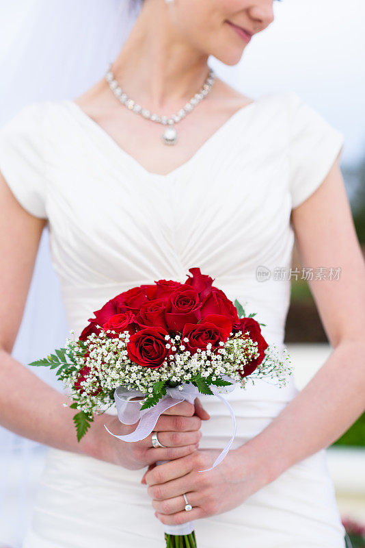 美丽的新娘拿着红色的花束在白色的礼服