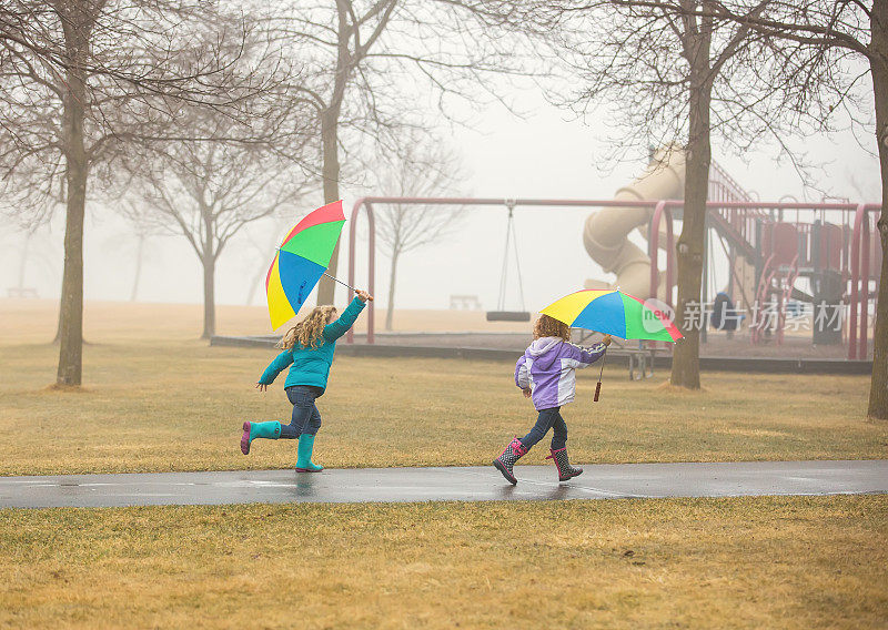 两个小女孩拿着雨伞在公园里跑步