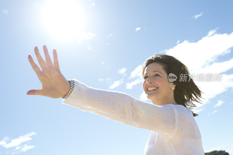 一个成熟的女人开心地微笑着，手伸向天空。