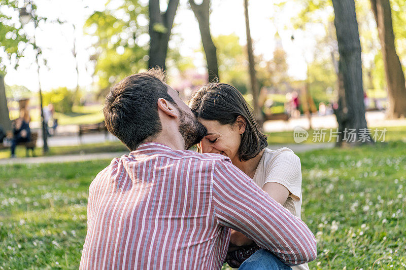 一对年轻夫妇正在公园里享受春天。他们在一起的时候，爱得更深。年轻的情侣在公园里微笑着拥抱。