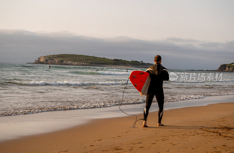日落或日出时，冲浪者带着冲浪板在海边散步。冲浪人的剪影寻找高浪。户外水上运动，度假和冒险的生活方式概念。