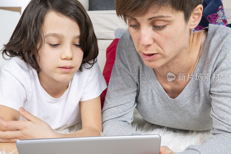 母亲和儿子躺在地毯上用数码平板电脑