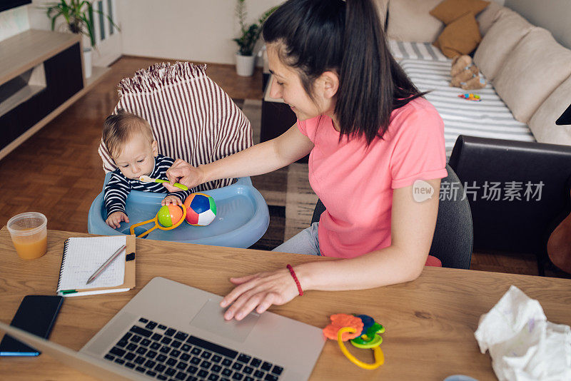 年轻的母亲一边在网上工作一边喂她的孩子