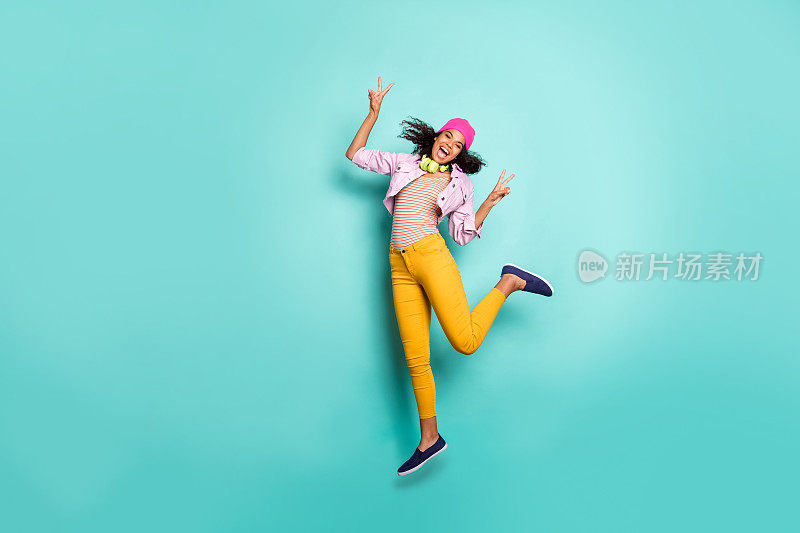 随意可爱的漂亮女孩跳跃的全身尺寸照片显示双v标志黄色长裤长裤帽子头饰粉色夹克条纹t恤兴奋孤立的生动的颜色蓝绿色背景