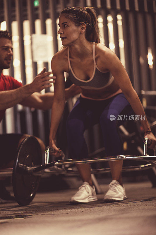 私人教练纠正年轻女性在健身房举重时的形态