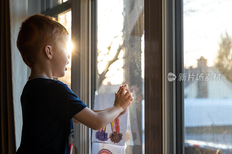 小男孩在日落时分把自己的画贴在家里的窗户上