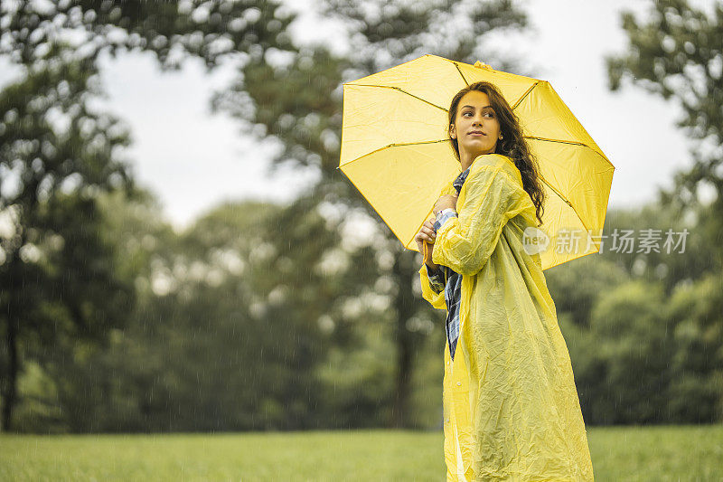 女人穿着雨衣，撑着雨伞，在雨天行走