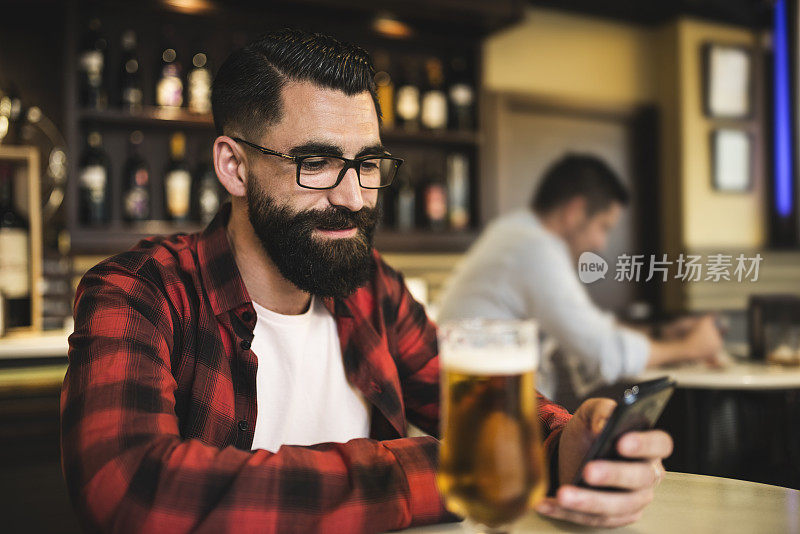 酒吧里的潮人喝着啤酒，摸着智能手机