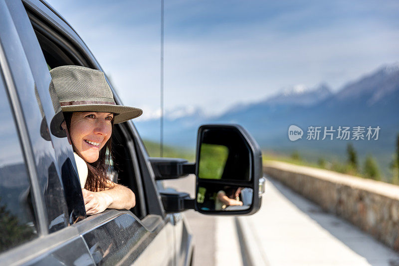 年轻时髦的女人靠在车窗上，一边开车一边欣赏风景