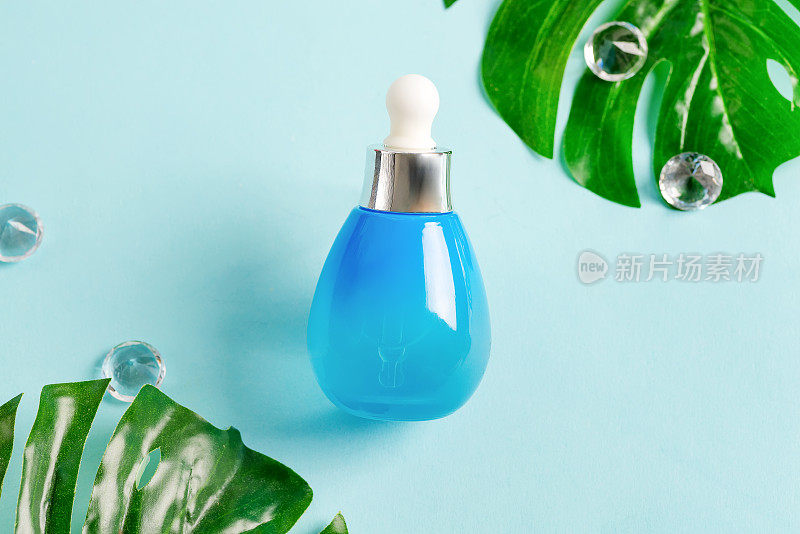 蓝色瓶子上有化妆品天然精油或乳液，淡蓝色背景上有热带绿叶。