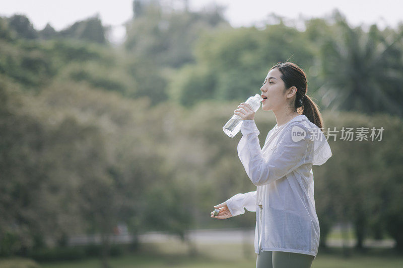 亚洲中国年轻女性在公园晨练后饮用玻璃瓶装水