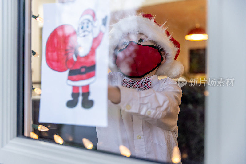 2019冠状病毒病大流行期间，一名小男孩在家里窗户上贴圣诞画