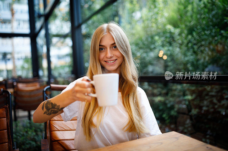 年轻的金发女子在咖啡馆喝咖啡