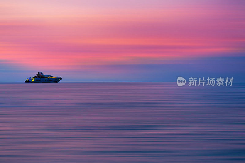 色彩斑斓的大海正面的观点日落与游艇在地平线上，运动模糊效果与土块和波浪。假期是放松和享受生活的时间。