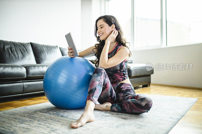 年轻运动女性的肖像与稳定球使用数字平板电脑在家里