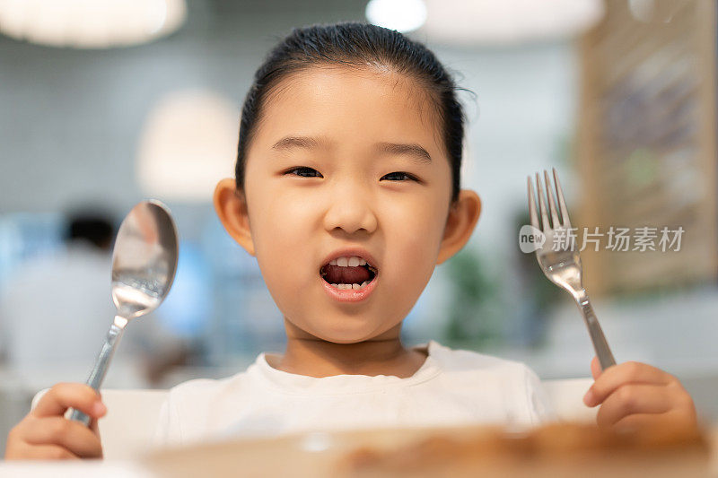 在餐厅里拿着勺子和叉子的可爱小女孩