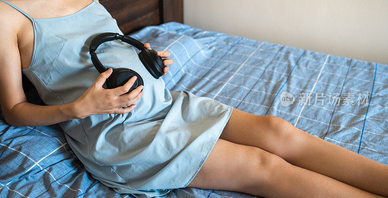 一名孕妇躺在床上，戴着耳机对着还在子宫里的婴儿玩