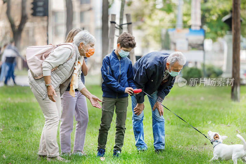 一对老年夫妇带着孙子孙女和一只可爱的狗在公园里散步。