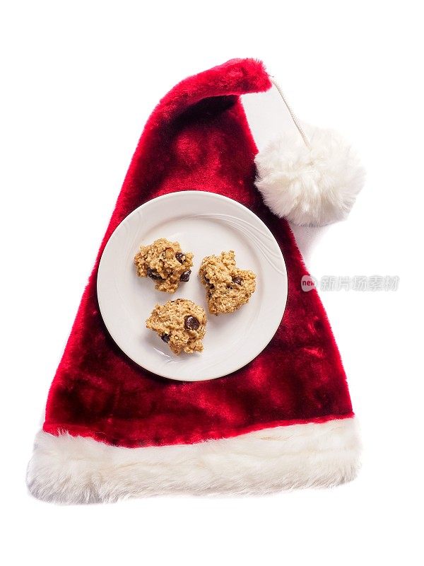 长毛绒的红色圣诞帽放在一盘自制的燕麦片、核桃和巧克力饼干旁边