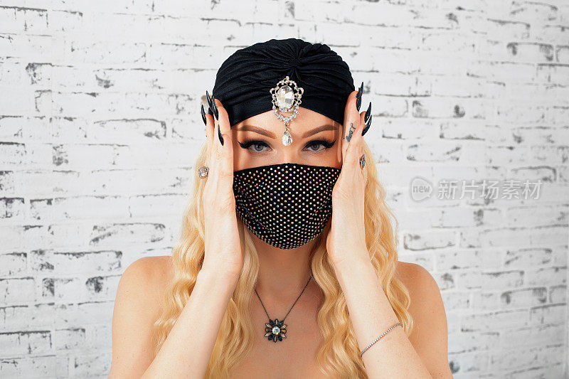 金发女人的肖像与美丽的化妆在黑色穆斯林头巾和黑色保护脸面具触摸脸与长黑色指甲