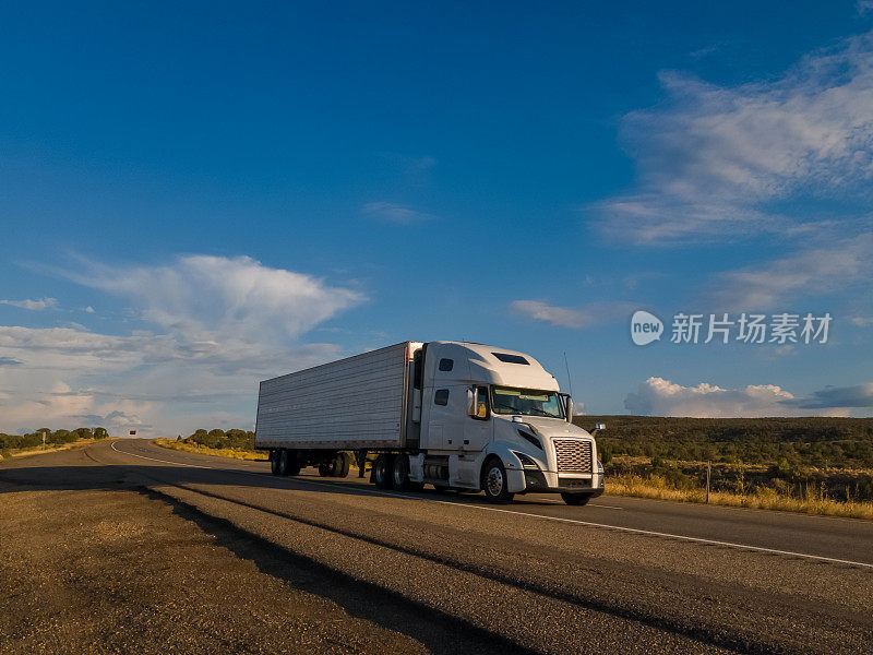 黄昏时分，在戏剧化的天空下，半卡车在犹他州沙漠的高速公路上超速行驶