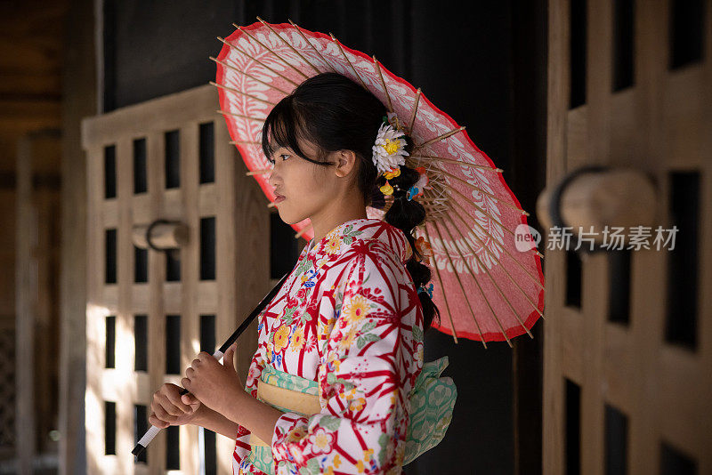 身穿和服、撑着纸伞的少女站在日本老房子前的照片