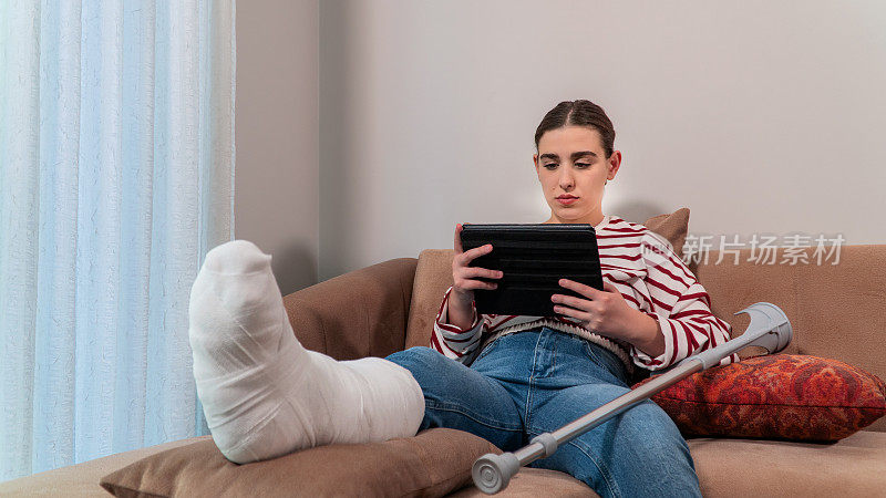 女孩，谁发生了事故，伤了她的腿，正坐在沙发上看平板电脑。