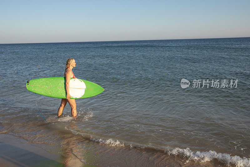 女人带着冲浪板走进宁静的大海