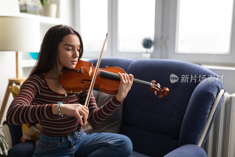 女小提琴手坐在舒适的沙发上练习拉小提琴。