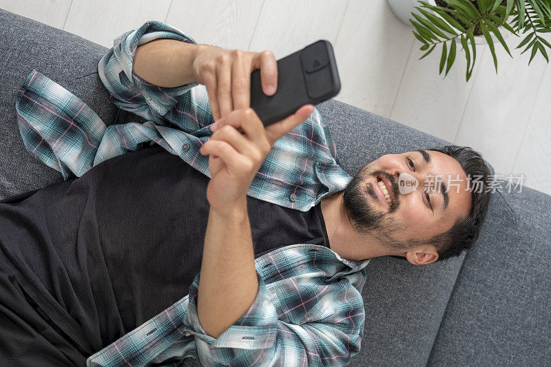 一个年轻人躺在沙发上用手机发短信