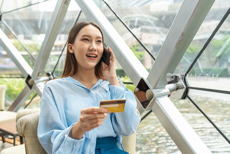 年轻聪明的亚洲女商人在蓝色寒意衬衫快乐地微笑在电话，当信用卡呼叫中心批准她的临时信用额度增加