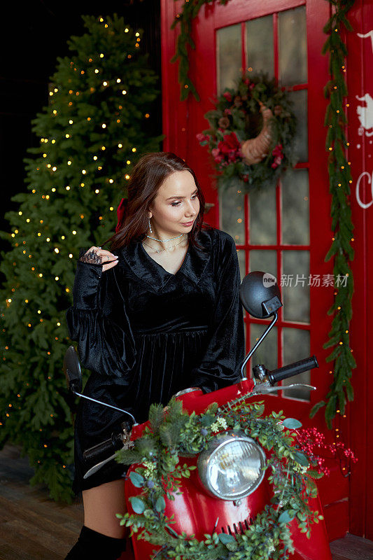 美女肖像上的一辆红色小摩托助动车，圣诞内饰。一个女人，一头美丽的长发，身穿黑色连衣裙，妆容自然