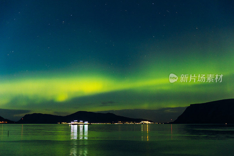 风景秀丽的北极光在峡湾和发光的城镇在挪威