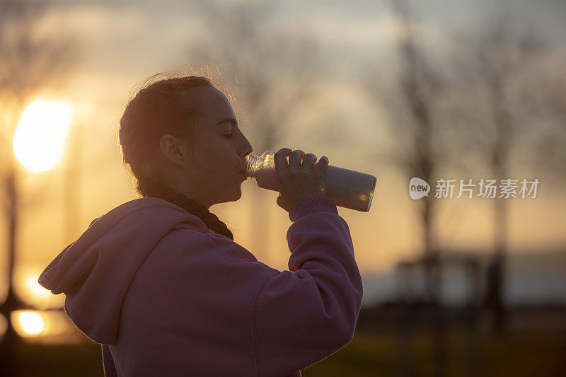 日落时分，一名年轻女子在公园慢跑时补水。