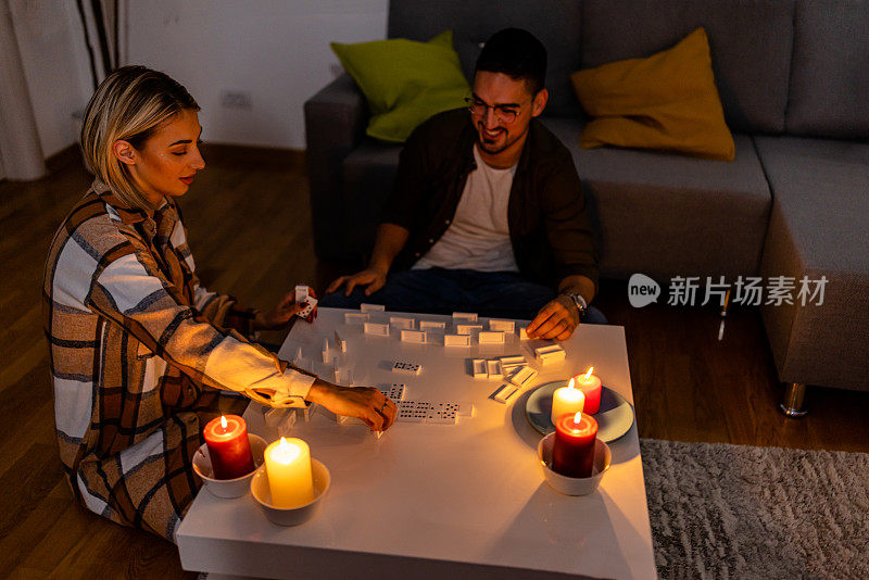 在一次精力充沛的危机中，一个男人和一个女人在黑暗中点燃蜡烛玩多米诺骨牌。