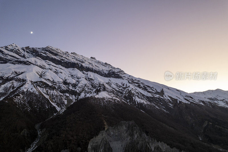 白雪皑皑的山峰映衬着彩色的日落天空。山上的日落