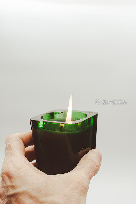 手拿白色背景的玻璃杯里的绿色香味蜡烛