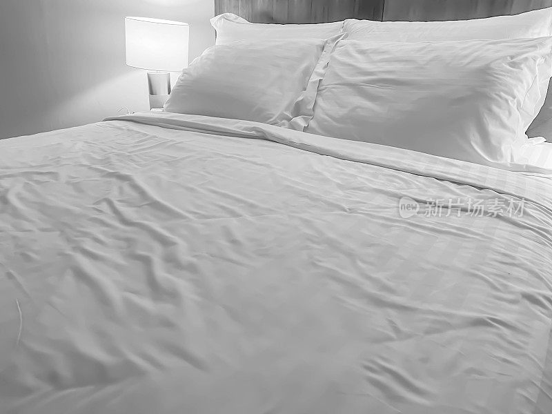 黑白色调的床上用品，褶皱的毛毯或羽绒被，枕头和卧室的灯光