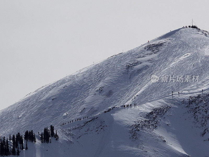 长焦视图数十名滑雪者和滑雪板徒步到12392英尺的高地峰滑雪碗。