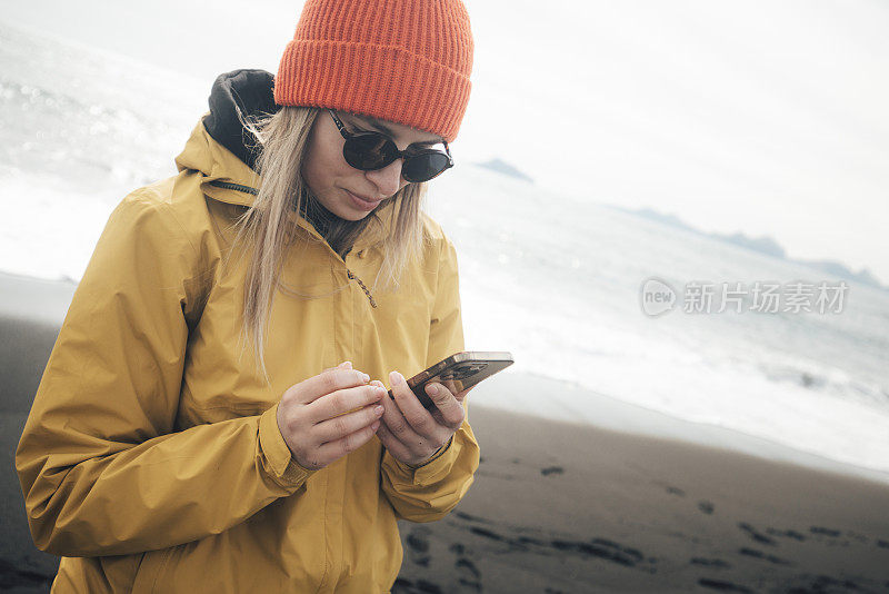 一名女子站在黑沙滩上玩手机。冰岛