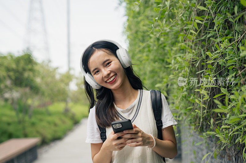 微笑的女人用智能手机和耳机拥抱大自然的旋律