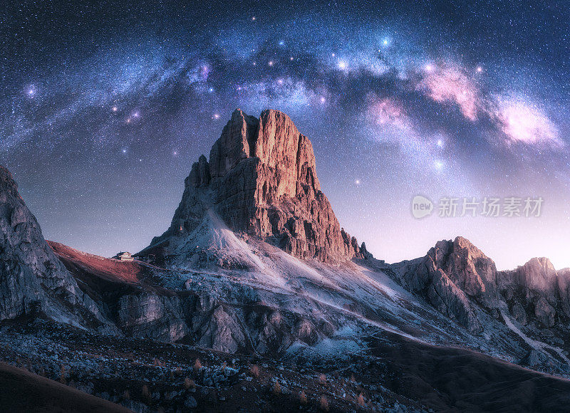银河横跨在美丽的岩石在繁星点点的夜晚，意大利白云石。紫色的天空，星星和明亮的拱形银河在高高的高山岩石之上。空间。自然