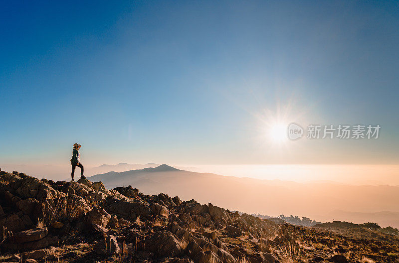 一个登山妇女的剪影在山顶上看日出